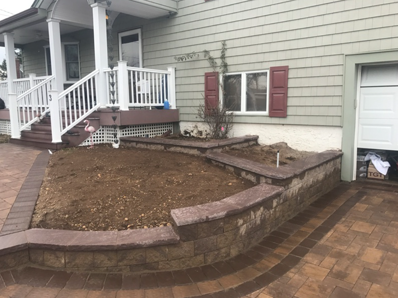 A house exterior with a curved brick retaining wall surrounding a dirt garden bed; brick walkway.