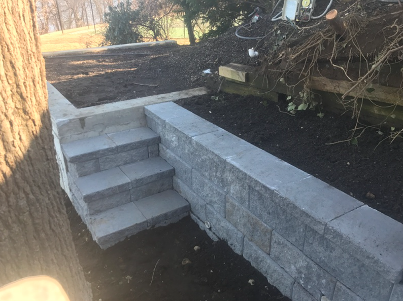Stone steps leading up from a retaining wall in a yard with freshly turned soil.