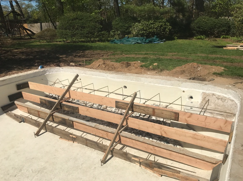 Pool under construction; wooden forms support rebar for steps. Concrete shell, outdoor setting.