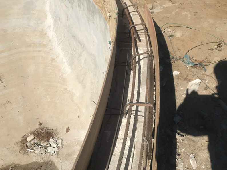 Concrete curved structure with exposed metal reinforcing bars, potentially a construction site.
