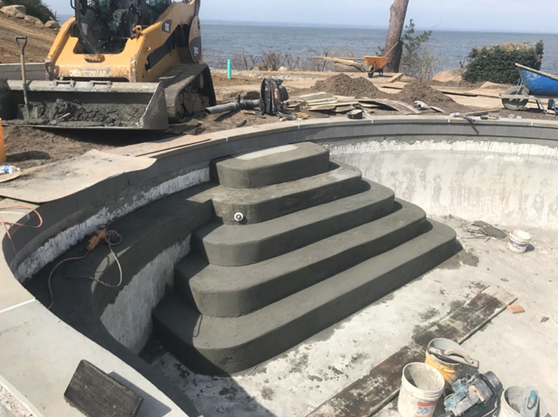 Construction of a concrete swimming pool with steps; heavy machinery is present.