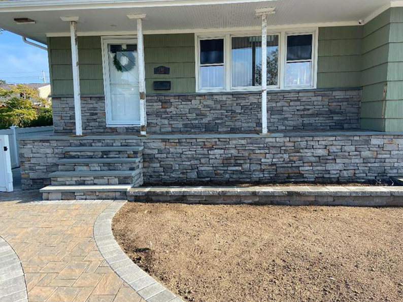 House exterior with stone facade, steps, and a paved walkway. Green siding, white door, and a bare lawn.