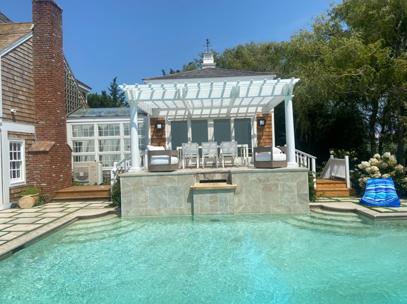 Swimming pool with pergola and outdoor seating, against a blue sky.