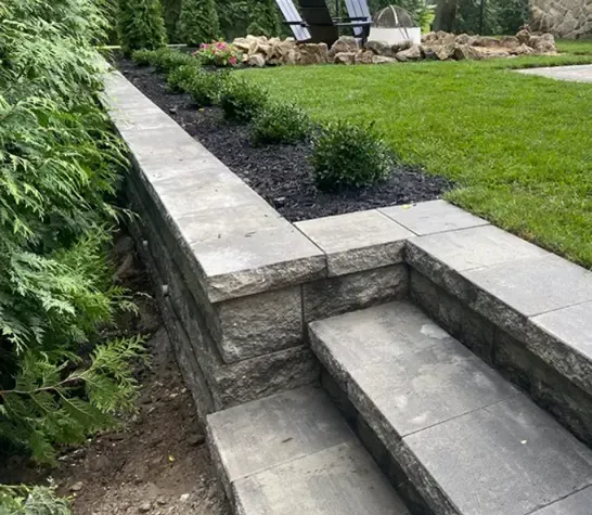 Stone steps lead up from a lawn to a raised garden bed with shrubs, next to a hedge.