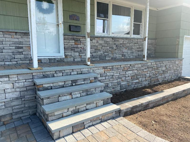 Stone facade house with steps, porch and walkway. Green siding, gray and brown stonework.