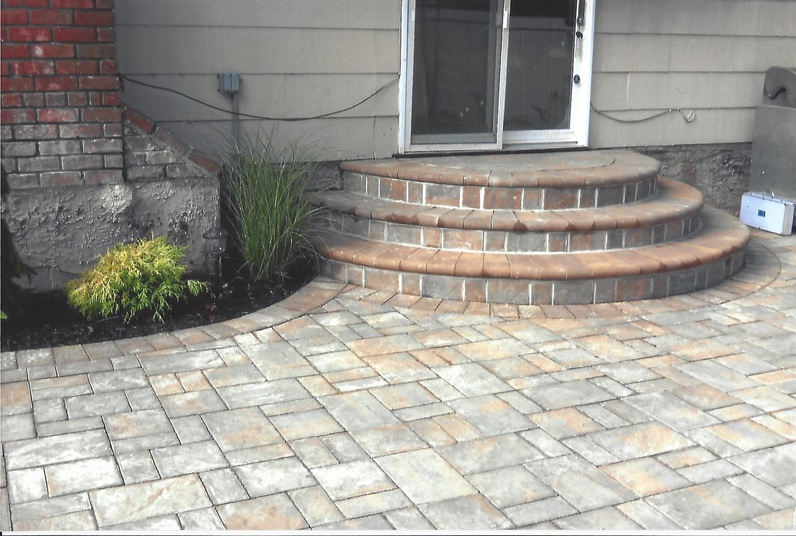Patio with brick steps leading to a sliding glass door. Landscaping with green plants.