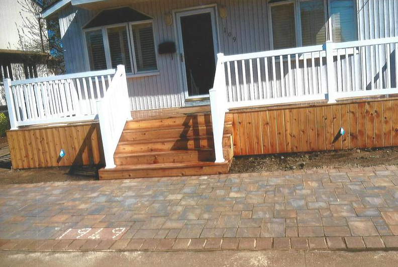 Wooden front porch with white railings, steps, and brick walkway.