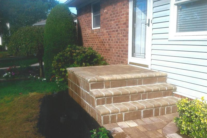 Brick steps leading to a house's front door, with a brick exterior and landscaping.