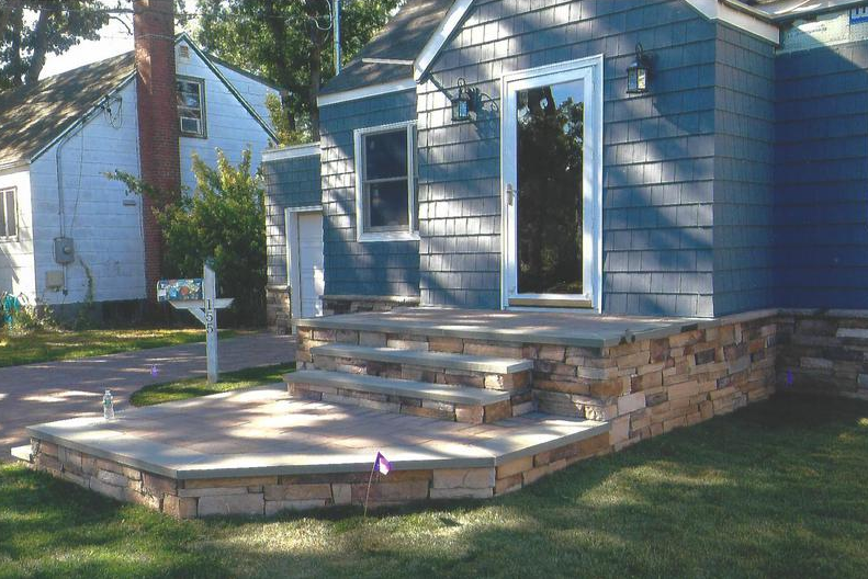 Blue house with stone steps leading to front door, lawn in foreground.