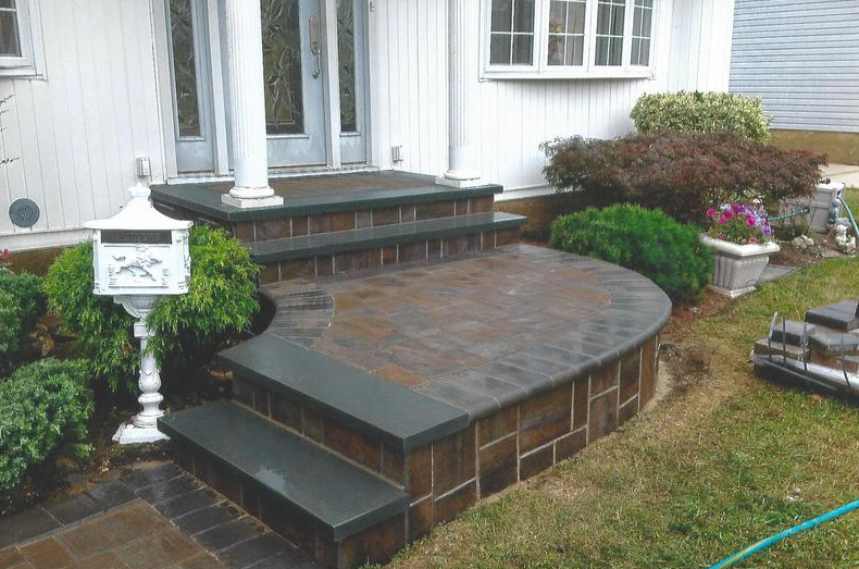 Brick steps and a curved landing lead to a house entrance.  Green bushes and a white mailbox are beside the steps.