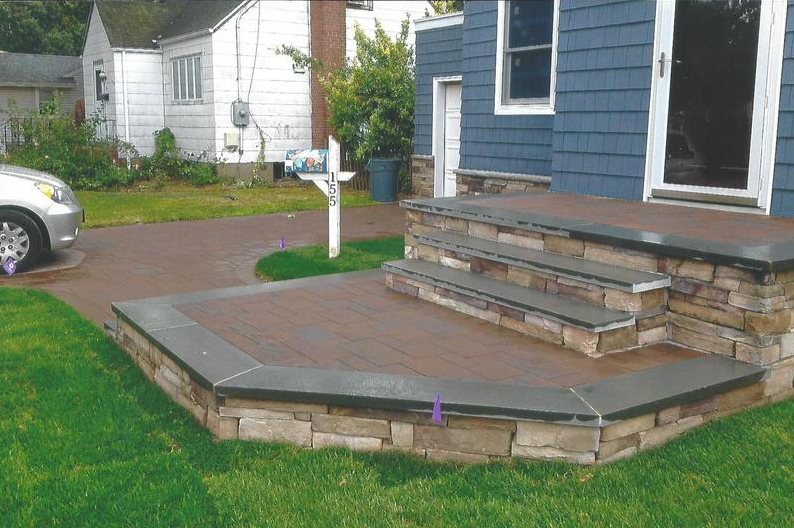 Blue house with stone steps leading to a composite deck and a driveway.