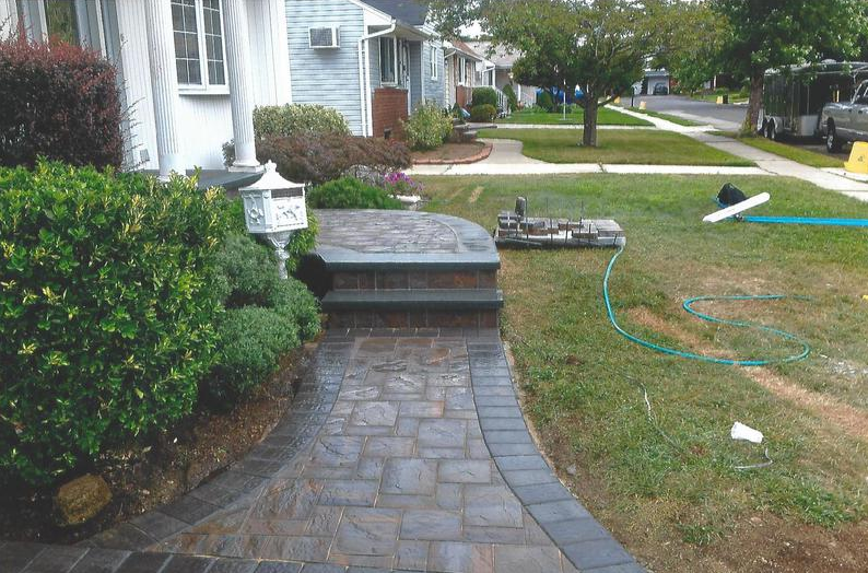 Brick pathway leading to house entrance with steps and landscaping.