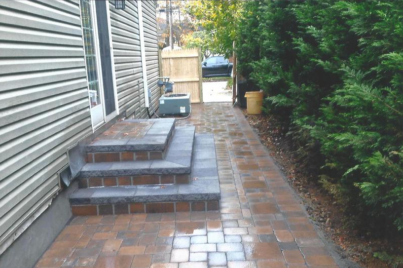Brick pathway with steps, leading from a house door towards a wooden gate.