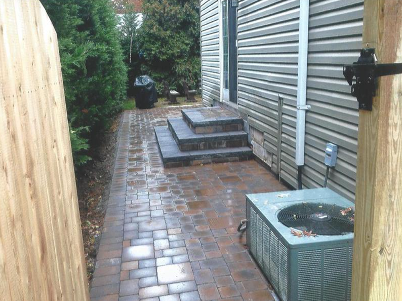 Brick pathway next to a house with steps leading to a door, air conditioning unit on the right.