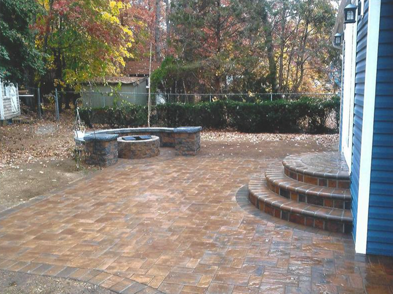 Backyard patio with brick pavers, fire pit, steps, and autumn foliage.