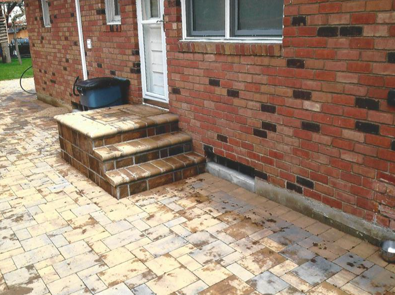 Brick steps and patio in front of a brick building with a white door.