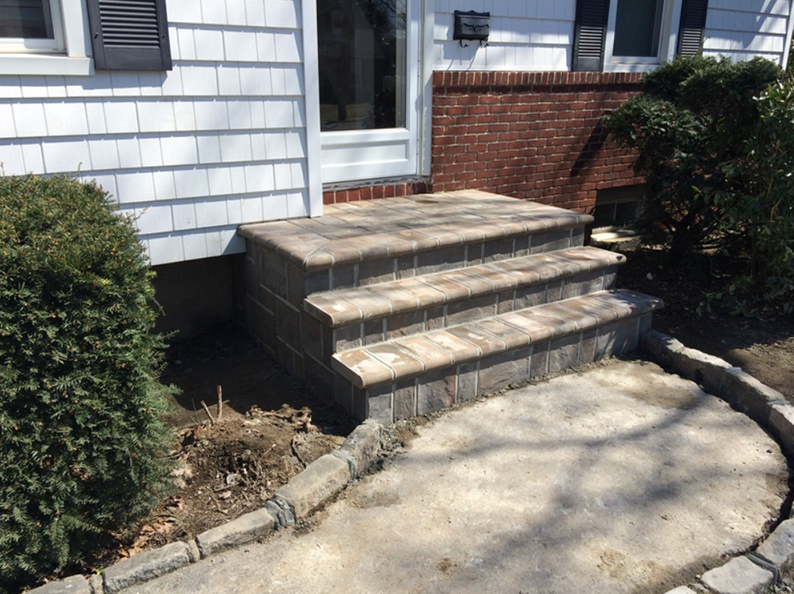 Brick steps leading up to a house entrance. Gray and brown bricks, with a circular brick walkway.