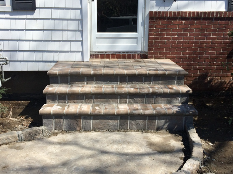 Brick steps leading up to a white door, next to a red brick wall.