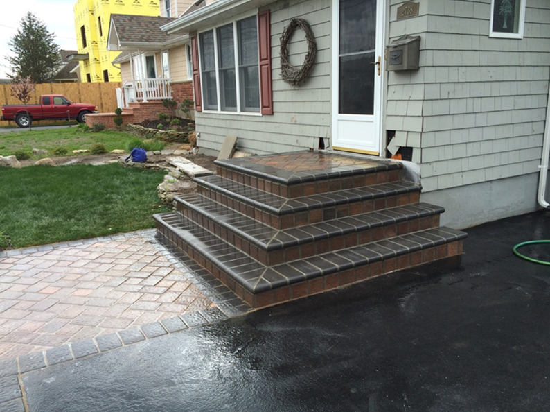 Brick steps leading to a house entrance with a brick paved walkway and a red pickup truck in the background.