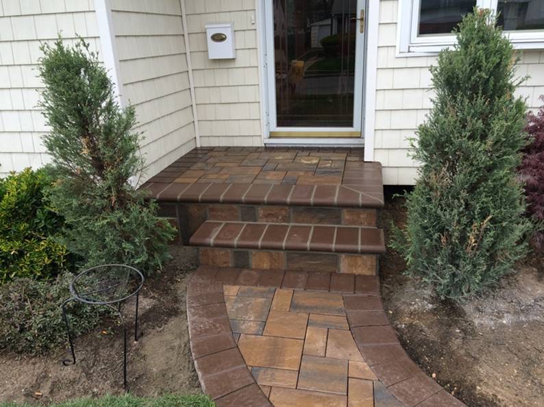 Brick steps leading to a front door, flanked by green bushes. A brick path leads to the steps.