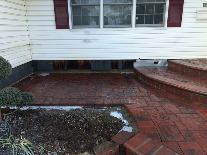 Brick patio and steps leading to a white house with a red shutter and window.