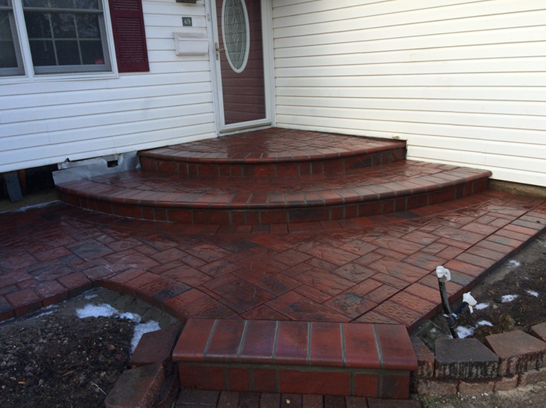 Brick steps and walkway leading to a house door with a red brick facade, partially covered in snow.