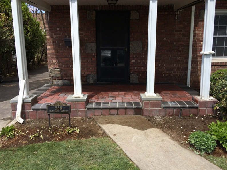 Brick front porch with steps leading to a dark door, supported by white columns.