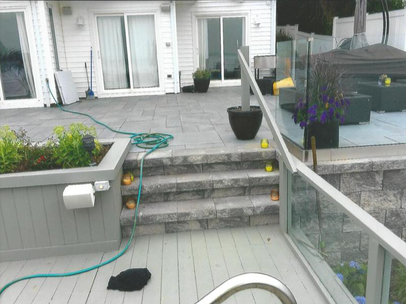 A deck with stone steps, planters, glass railings, and a house in the background. Several tennis balls are visible.
