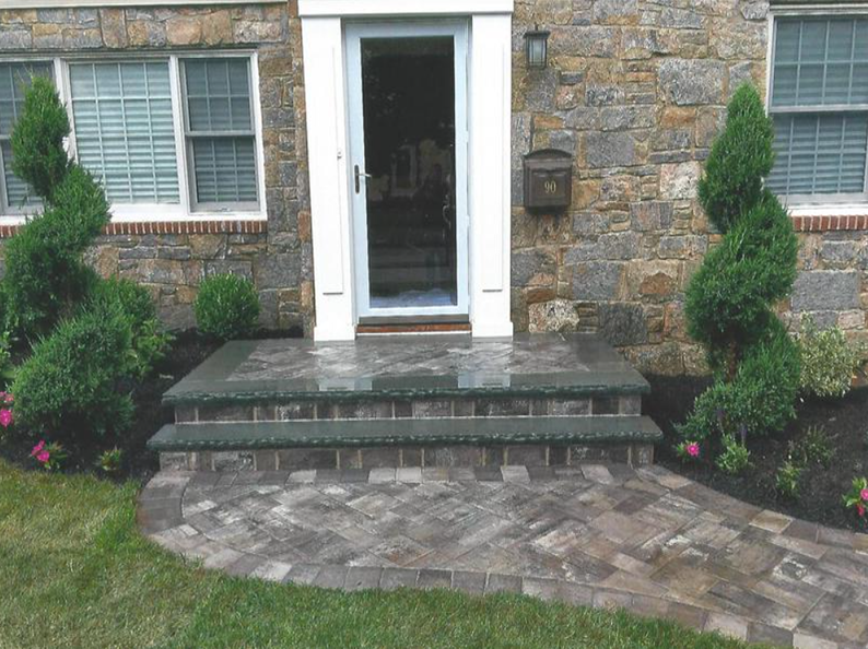 Stone steps and walkway leading to a front door with spiral bushes on either side of the entrance.