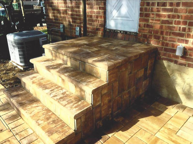 Brick steps leading up to a brick platform and door. An air conditioning unit sits on the left.