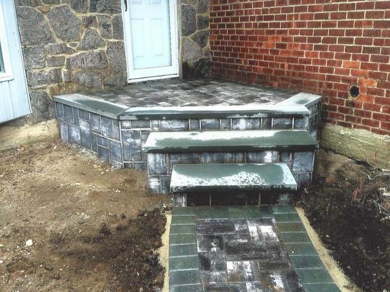 Brick steps leading to a house entrance, with a brick path, granite stone wall, and red brick wall.