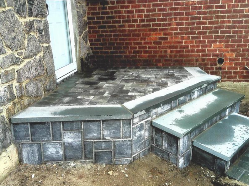 Stone steps and landing leading to a door on a building with a brick wall.