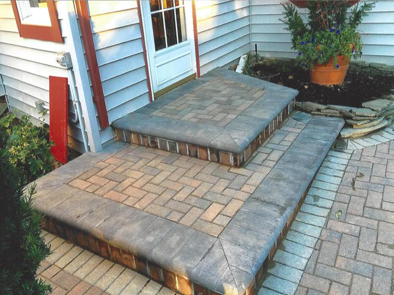 Brick steps with a gray border lead to a white door. A potted plant sits nearby.