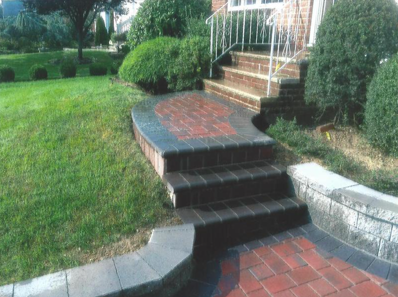 Brick steps leading to a house entrance, bordered by a brick patio and green lawn.