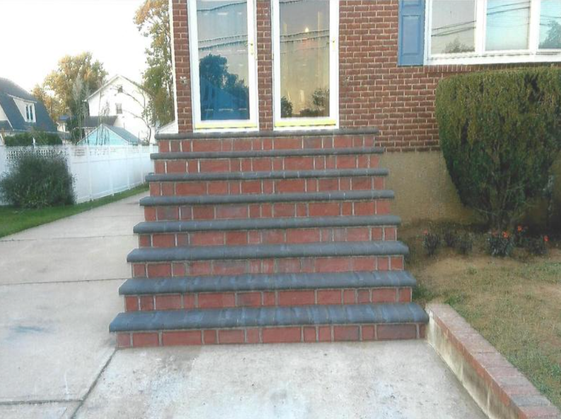 Brick steps leading up to a house entrance with glass doors and blue shutters.