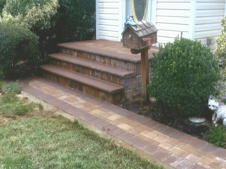 Brick steps and walkway leading to a house entrance with a mailbox and shrubbery.