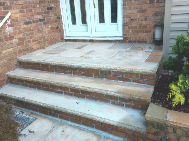 Brick steps leading up to white double doors, framed by red brick, with a sandstone-colored landing and trim.