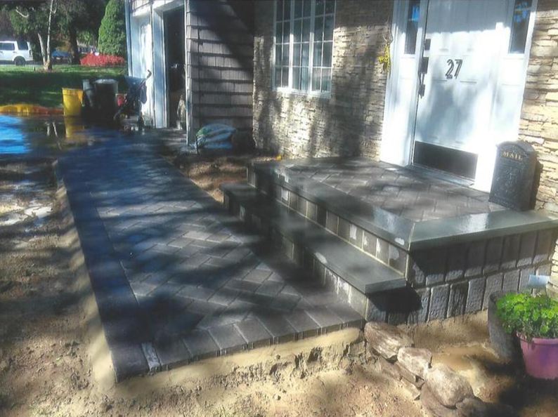 A newly constructed brick walkway and steps leading to a home's front door, with fresh landscaping.