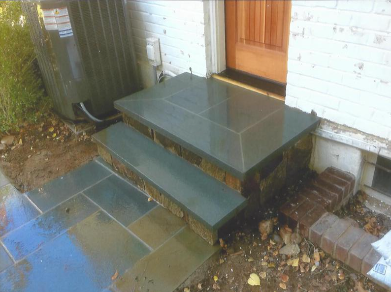 Stone steps leading to a door with a newly paved walkway; a/c unit on the left.