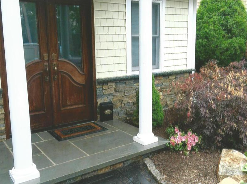 A home's entrance with brown double doors, white pillars, stone steps, and a small garden.