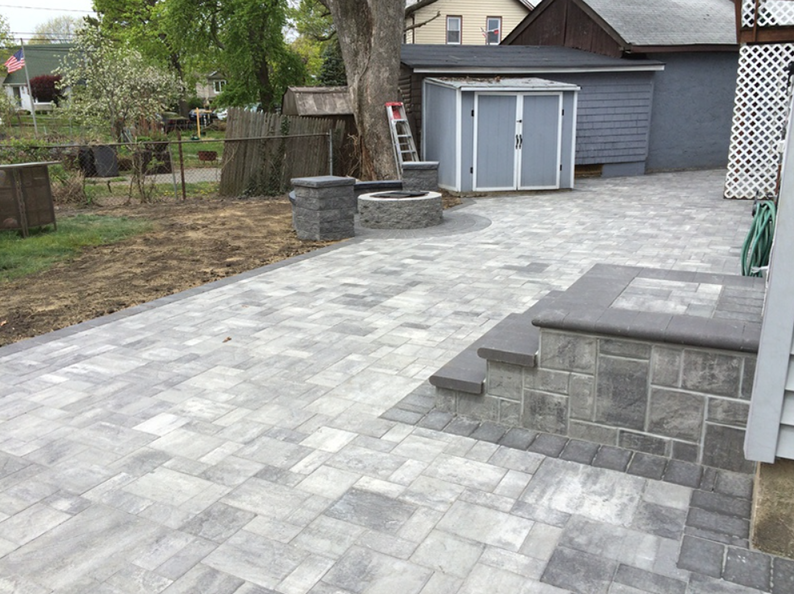 Backyard patio with gray pavers and stone steps, fire pit, and shed.