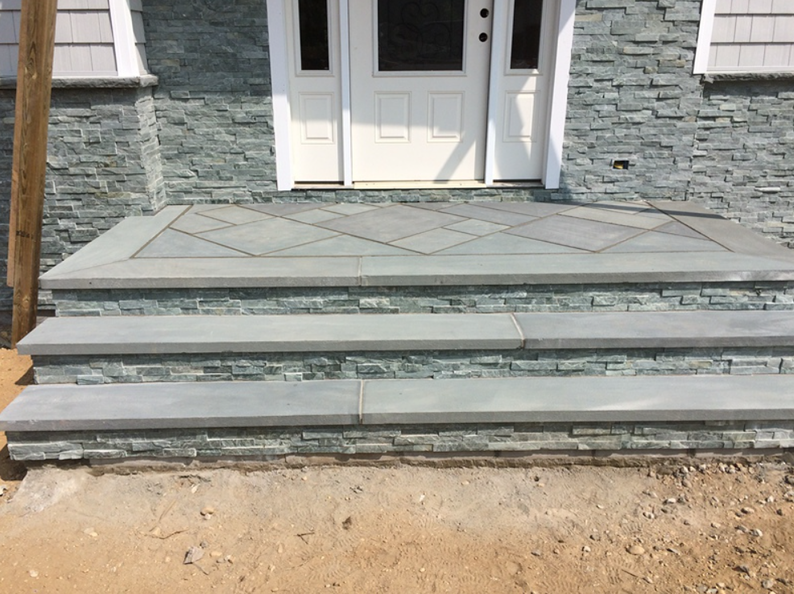 Stone steps lead to a white door. Blue stone veneer surrounds the entrance.