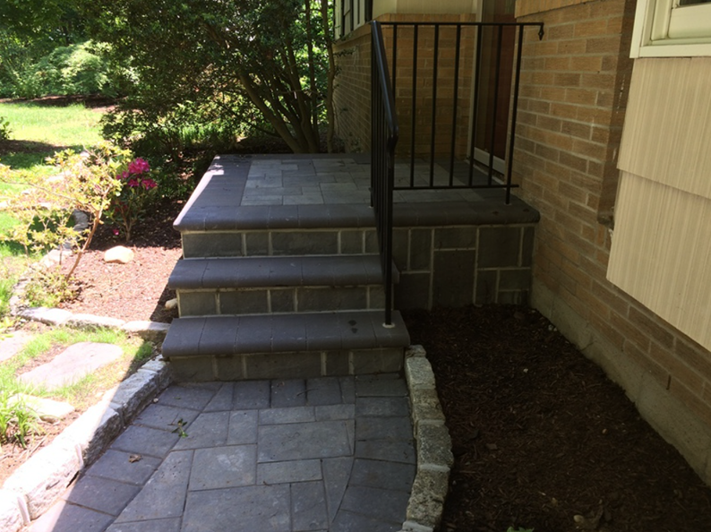 Stone steps leading to a brick house entrance with black railing and fresh mulch.