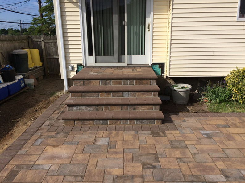Stone steps leading to a sliding glass door on a yellow house. Paver patio in foreground.