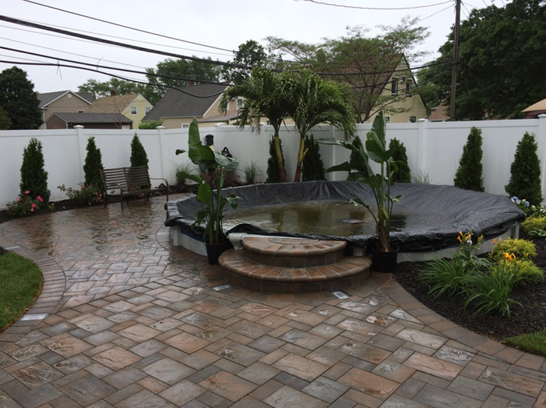 Patio with paver stones, above-ground pool covered in black tarp, white fence, and landscaping.