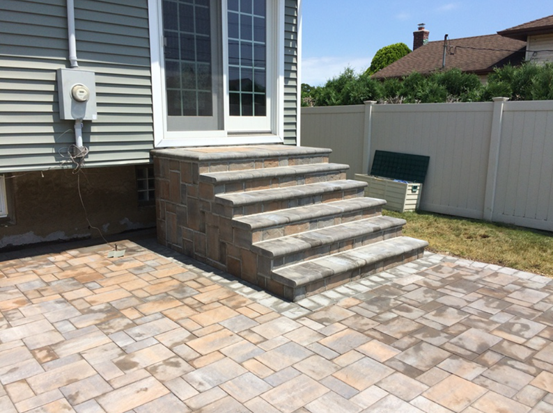 Brick steps leading to a sliding glass door on a gray-sided house, with a brick patio in front.