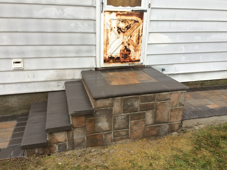 Three concrete steps leading to a weathered brown door. Stone facade on step base.