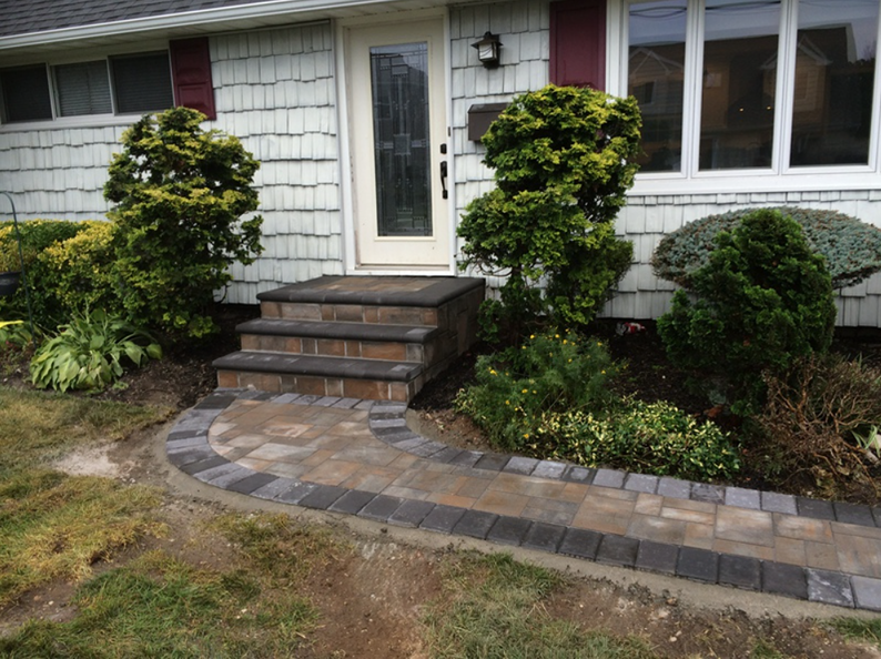 Brick path and steps leading to a house entrance with bushes and greenery.