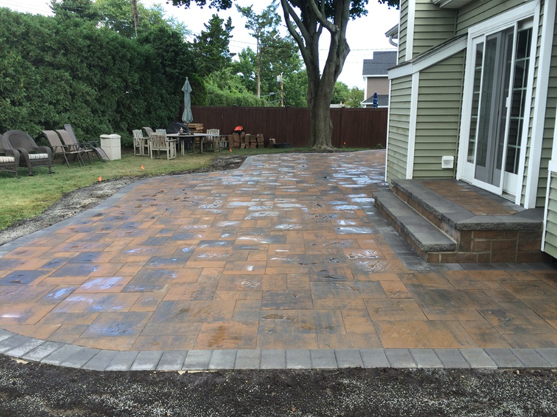 Brick patio next to a house with steps and a garden.