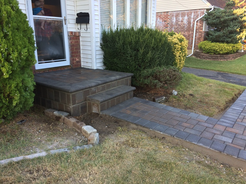 Brick steps and walkway leading to a house entrance, bordered by grass and shrubs.